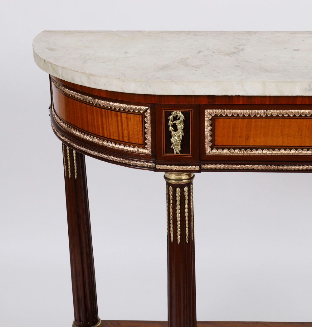 A pair of 19th-century French Louis XVI style demi-lune console tables with white Carrara marble tops, gilt bronze mounts, fluted legs, and undershelves. View XIV