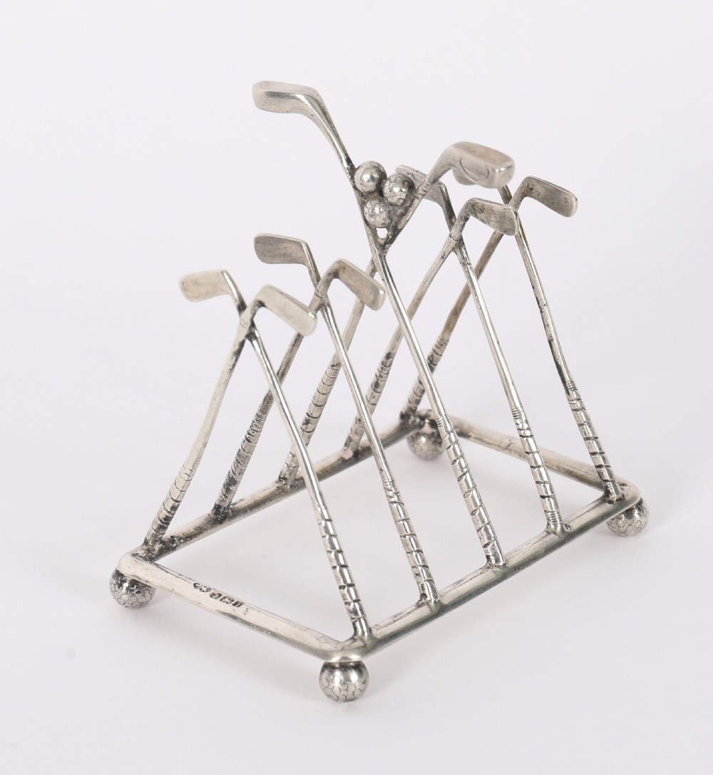 An Edwardian sterling silver toast rack formed from crossed golf clubs resting on small golf ball feet.