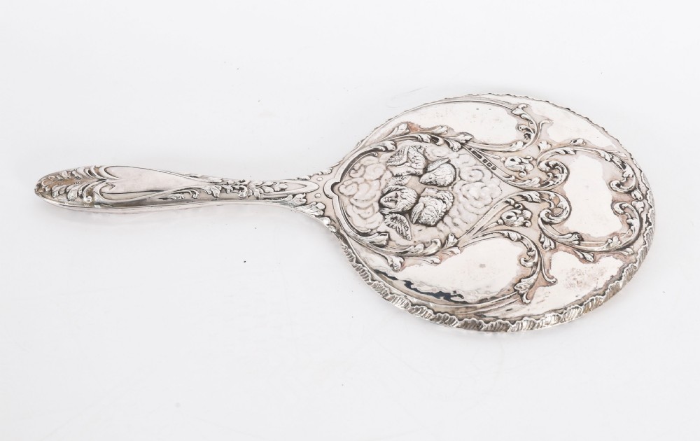 An Edwardian sterling silver hand mirror decorated with high-relief repousse cherubs amidst clouds and scrollwork. View IX
