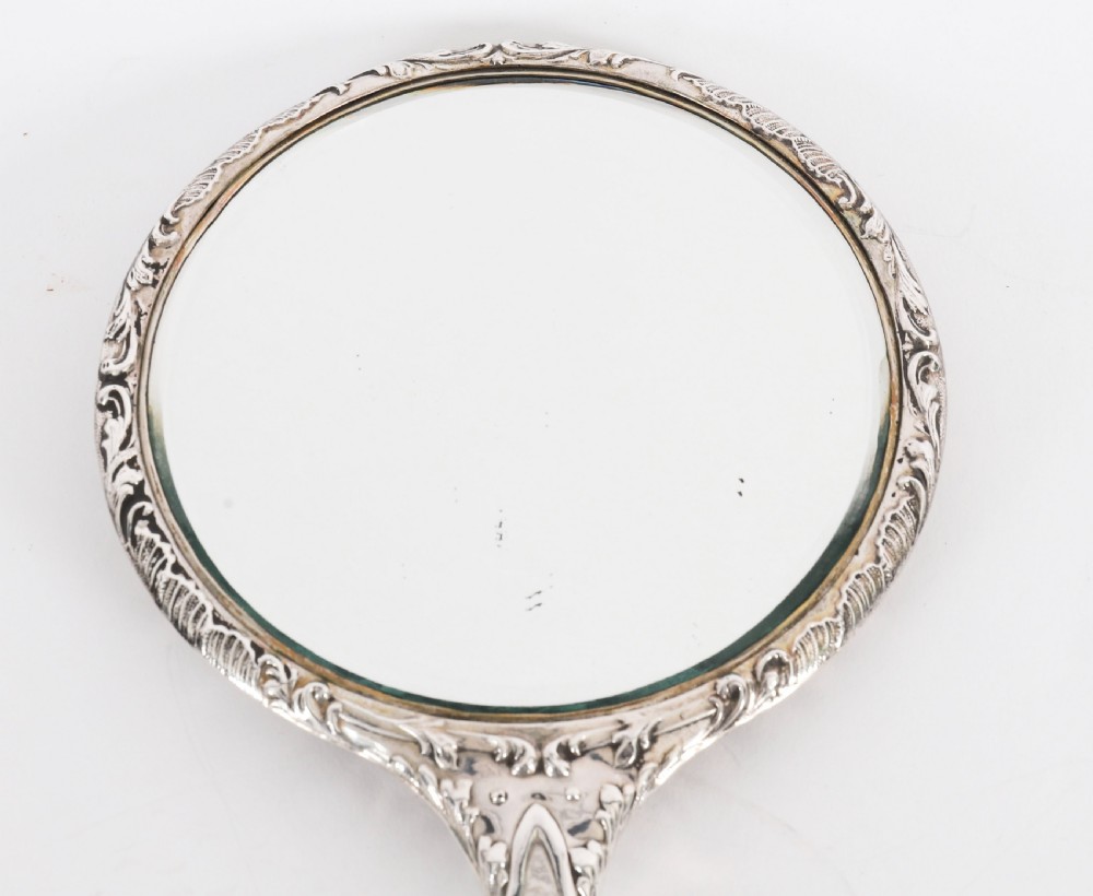 An Edwardian sterling silver hand mirror decorated with high-relief repousse cherubs amidst clouds and scrollwork. View XII