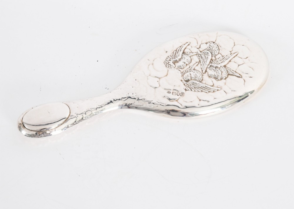 An Edwardian sterling silver hand mirror featuring embossed cherub heads and clouds on the back.