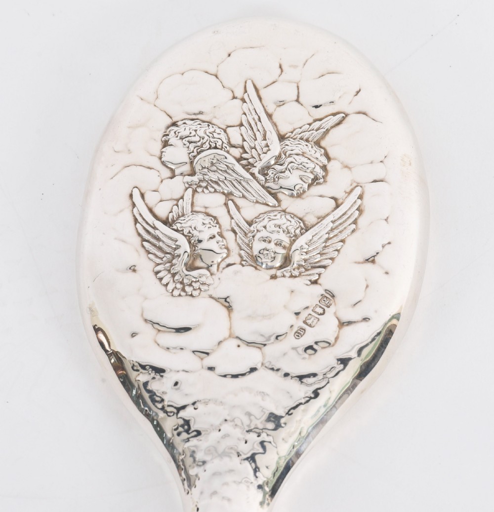 An Edwardian sterling silver hand mirror featuring embossed cherub heads and clouds on the back. View IV