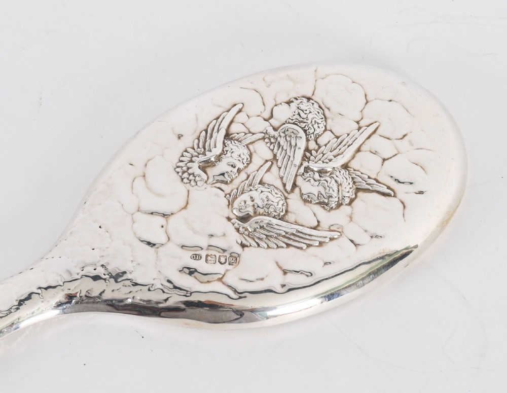 An Edwardian sterling silver hand mirror featuring embossed cherub heads and clouds on the back. View VII