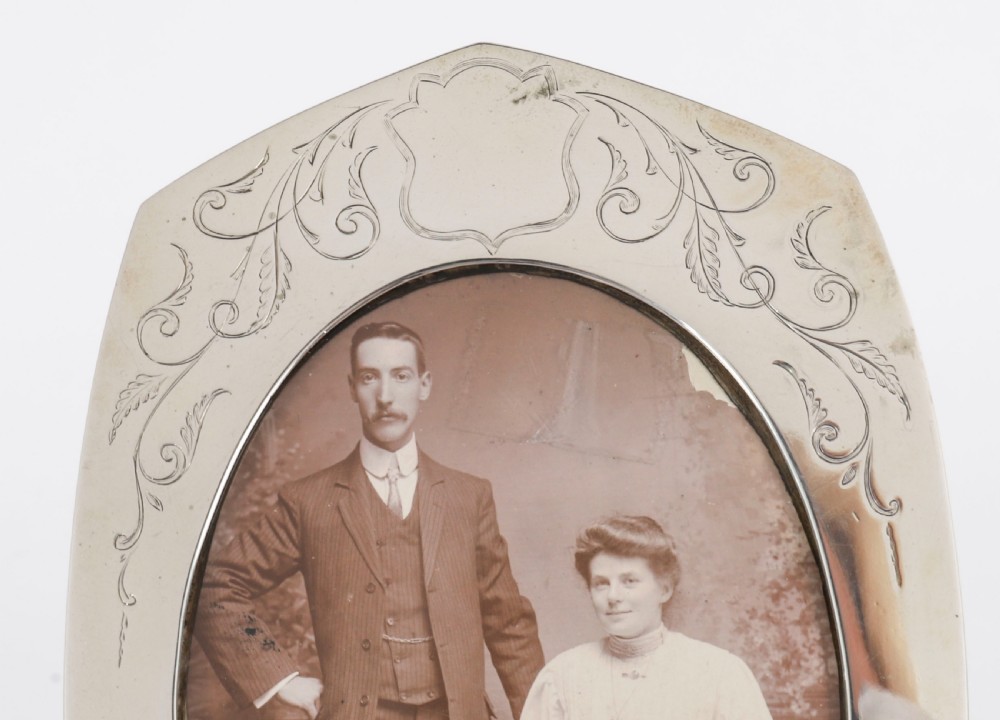 An arched sterling silver photo frame featuring engraved floral motifs around an oval picture aperture. View VIII