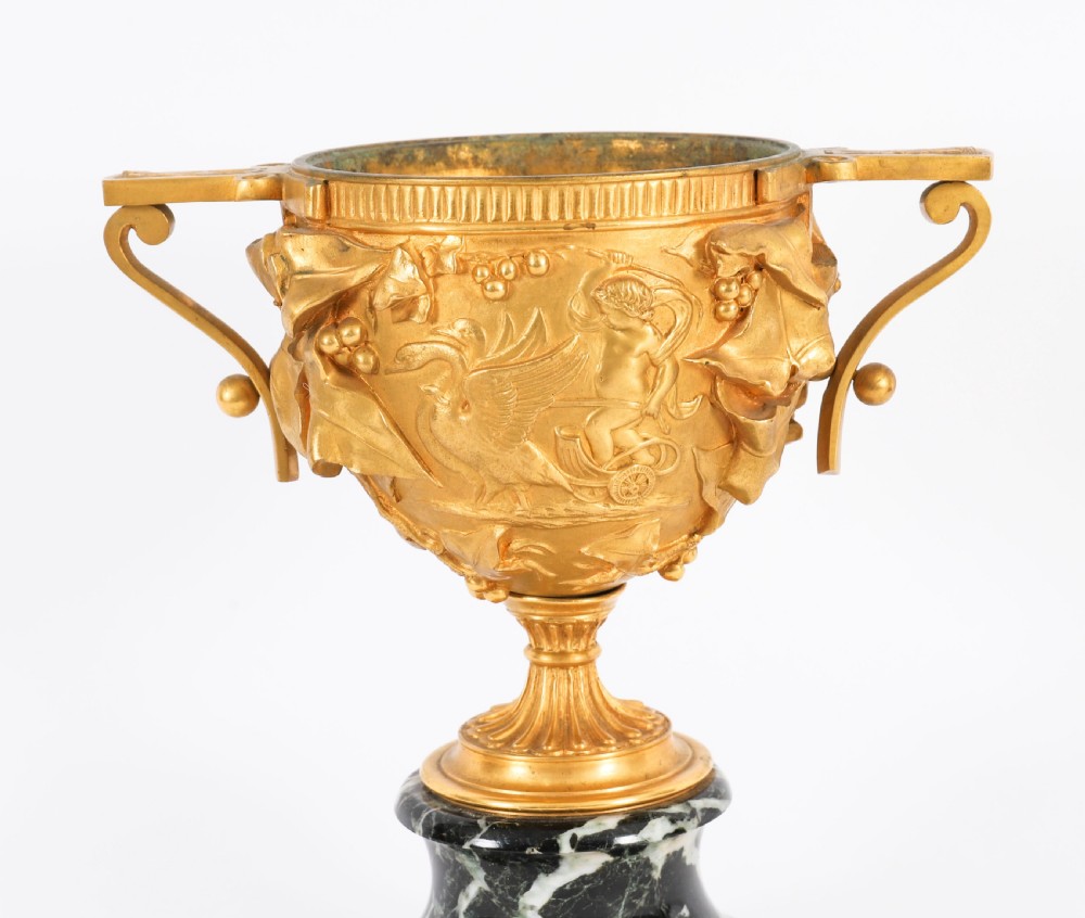 A pair of nineteenth-century French gilt bronze classical urns featuring relief carvings and scroll handles, mounted on dark green marble bases. View III