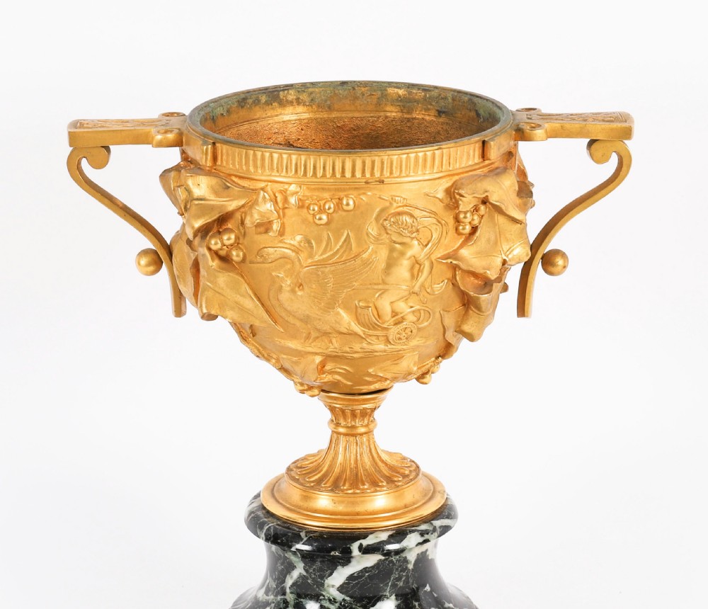 A pair of nineteenth-century French gilt bronze classical urns featuring relief carvings and scroll handles, mounted on dark green marble bases. View VII