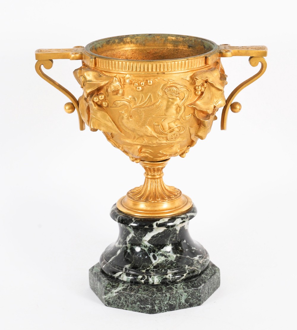 A pair of nineteenth-century French gilt bronze classical urns featuring relief carvings and scroll handles, mounted on dark green marble bases. View IX