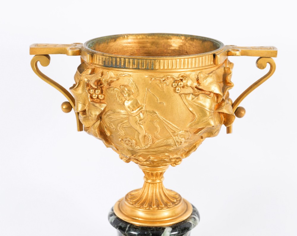 A pair of nineteenth-century French gilt bronze classical urns featuring relief carvings and scroll handles, mounted on dark green marble bases. View XIII