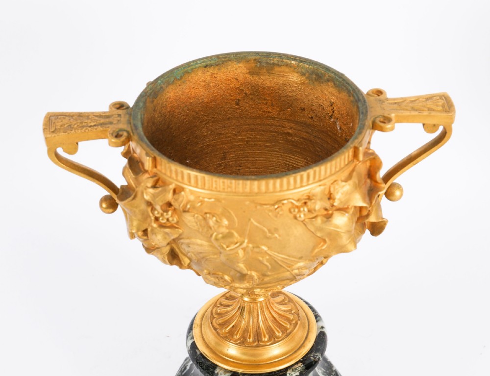 A pair of nineteenth-century French gilt bronze classical urns featuring relief carvings and scroll handles, mounted on dark green marble bases. View XVII