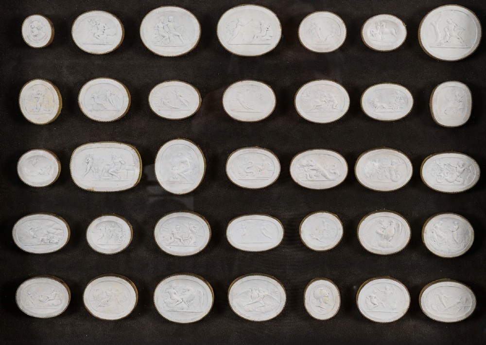A framed display of thirty-five off-white plaster intaglio impressions featuring classical relief figures mounted on a dark background within a gilt frame. View III