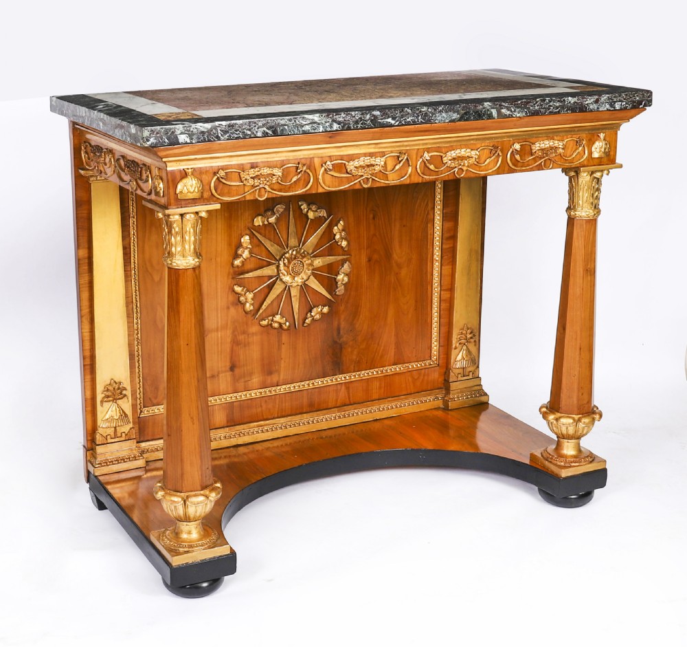 A French Empire walnut console table with a dark marble top, gold parcel gilt column supports, and a starburst motif panel.
