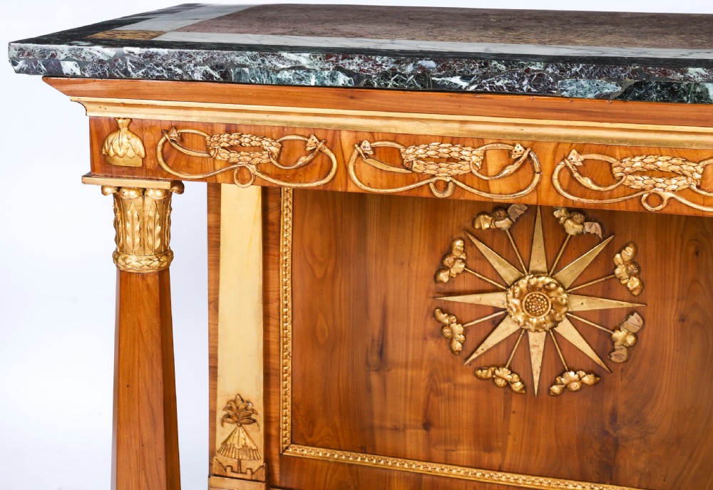 A French Empire walnut console table with a dark marble top, gold parcel gilt column supports, and a starburst motif panel. View VIII