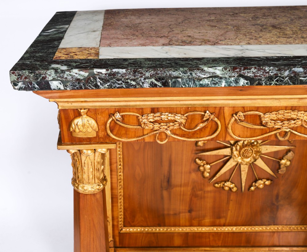 A French Empire walnut console table with a dark marble top, gold parcel gilt column supports, and a starburst motif panel. View X