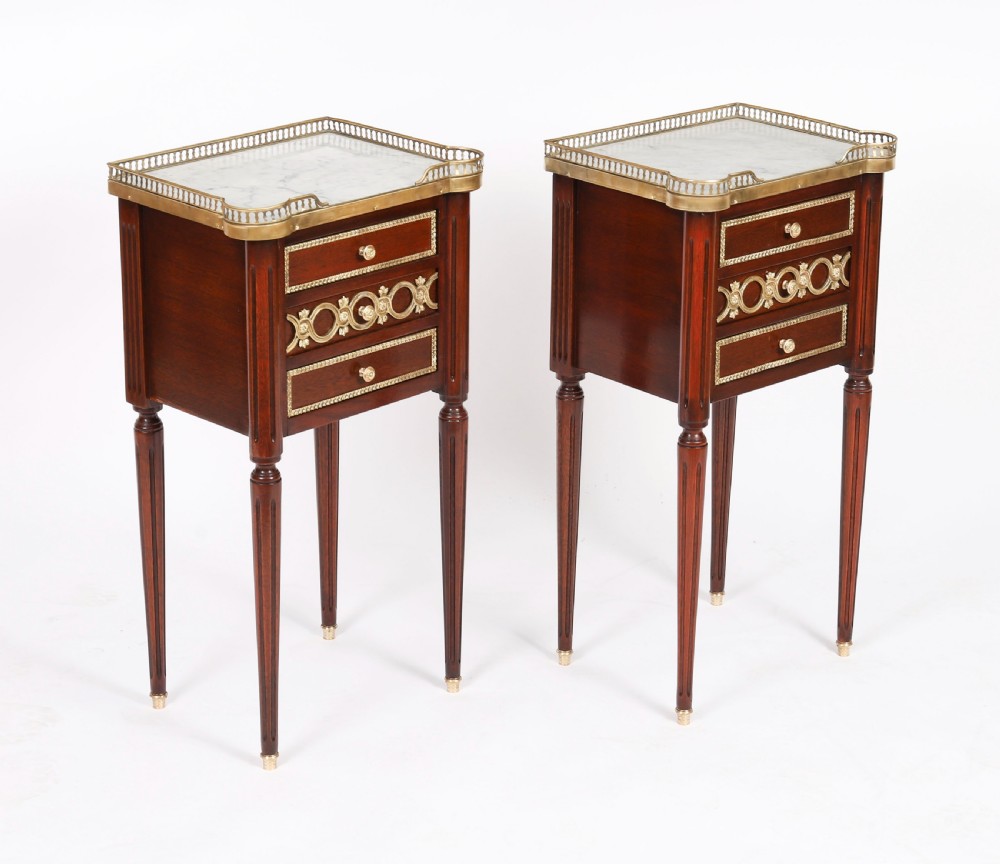 A pair of 19th-century mahogany French Empire bedside cabinets featuring white marble tops with pierced brass galleries, gilt bronze mounts, and slender fluted legs. View II