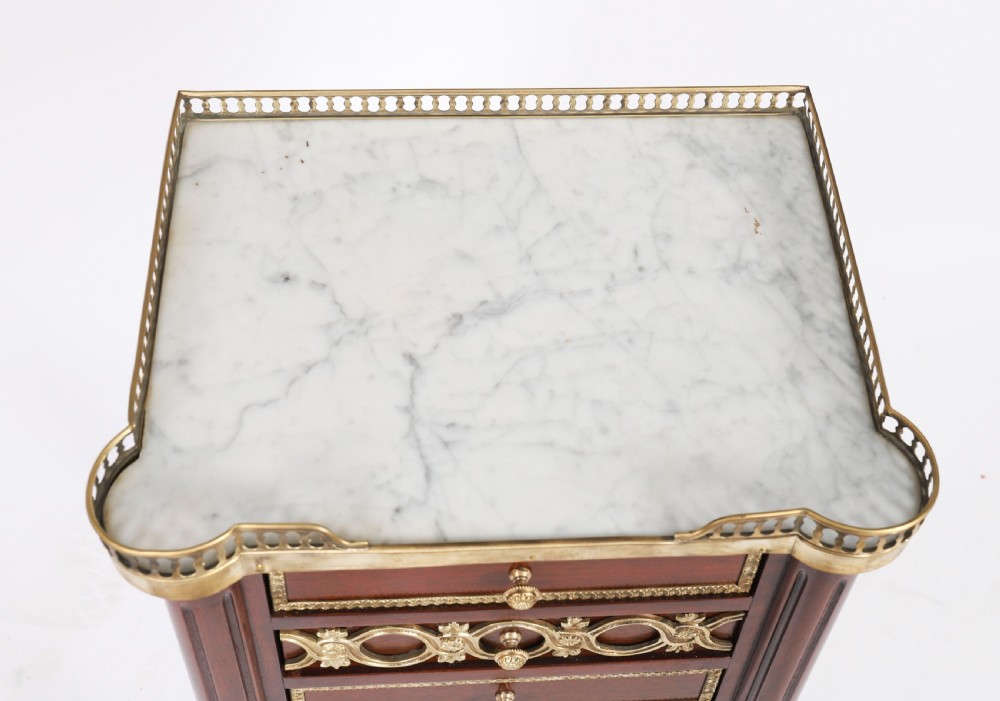 A pair of 19th-century mahogany French Empire bedside cabinets featuring white marble tops with pierced brass galleries, gilt bronze mounts, and slender fluted legs. View V