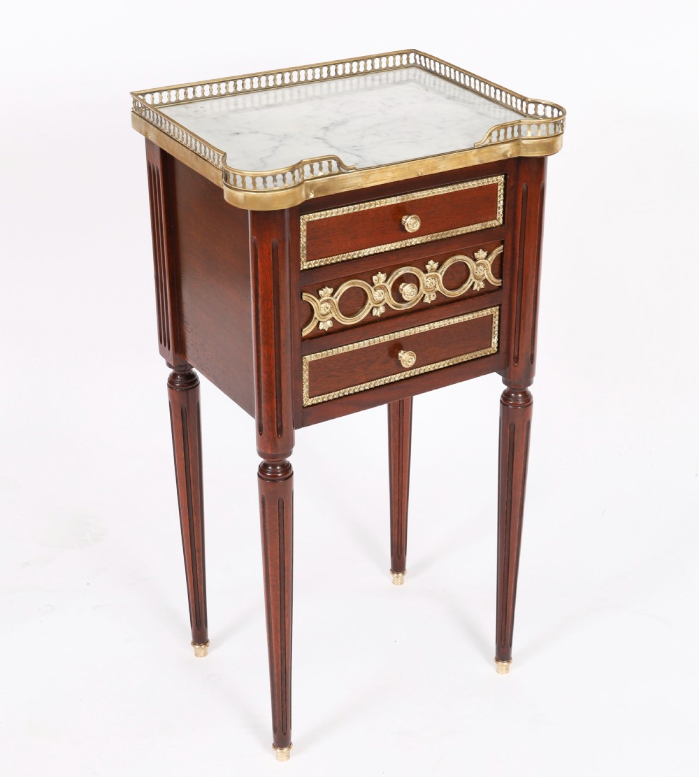 A pair of 19th-century mahogany French Empire bedside cabinets featuring white marble tops with pierced brass galleries, gilt bronze mounts, and slender fluted legs. View VI