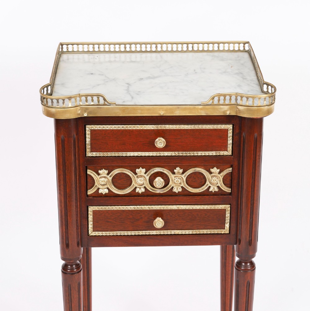 A pair of 19th-century mahogany French Empire bedside cabinets featuring white marble tops with pierced brass galleries, gilt bronze mounts, and slender fluted legs. View IX
