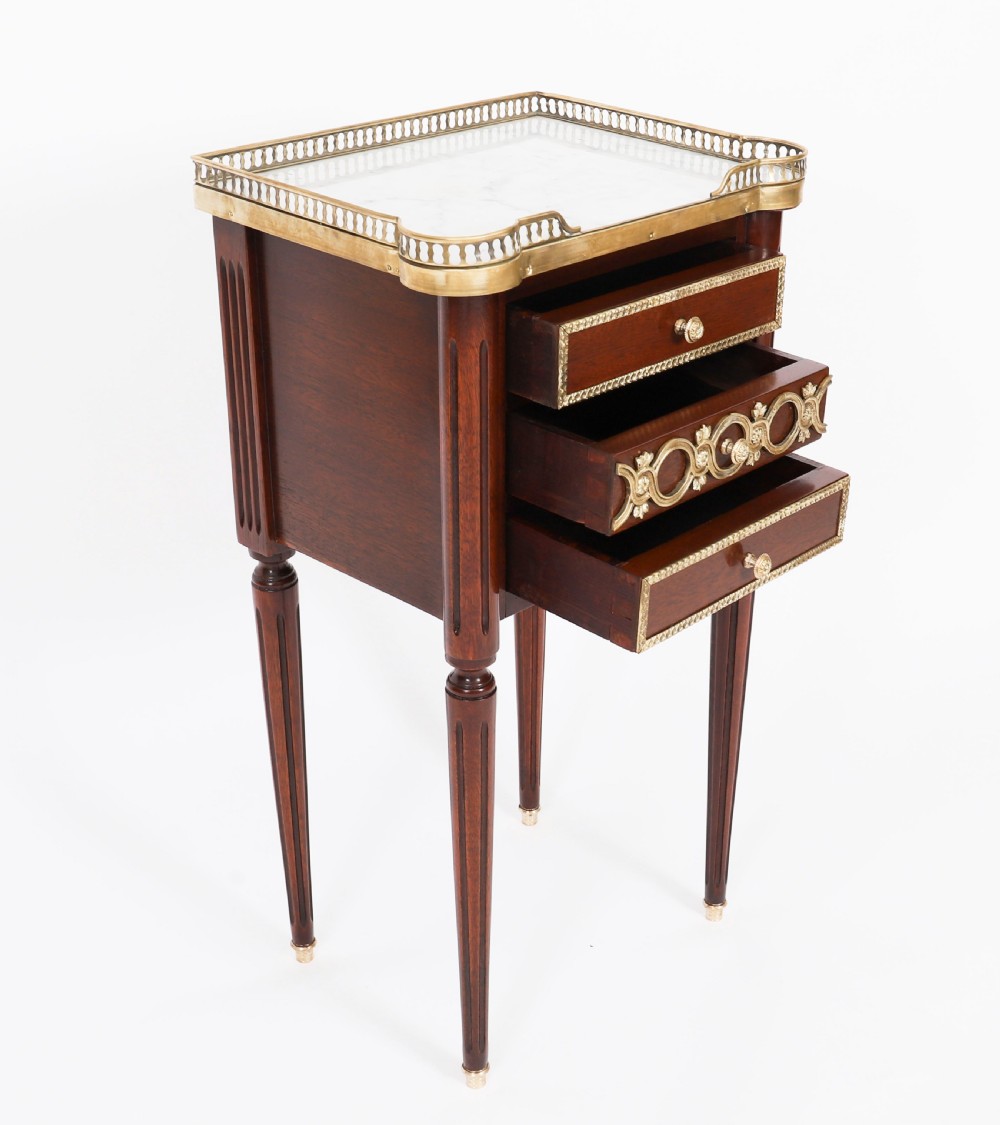 A pair of 19th-century mahogany French Empire bedside cabinets featuring white marble tops with pierced brass galleries, gilt bronze mounts, and slender fluted legs. View XIV