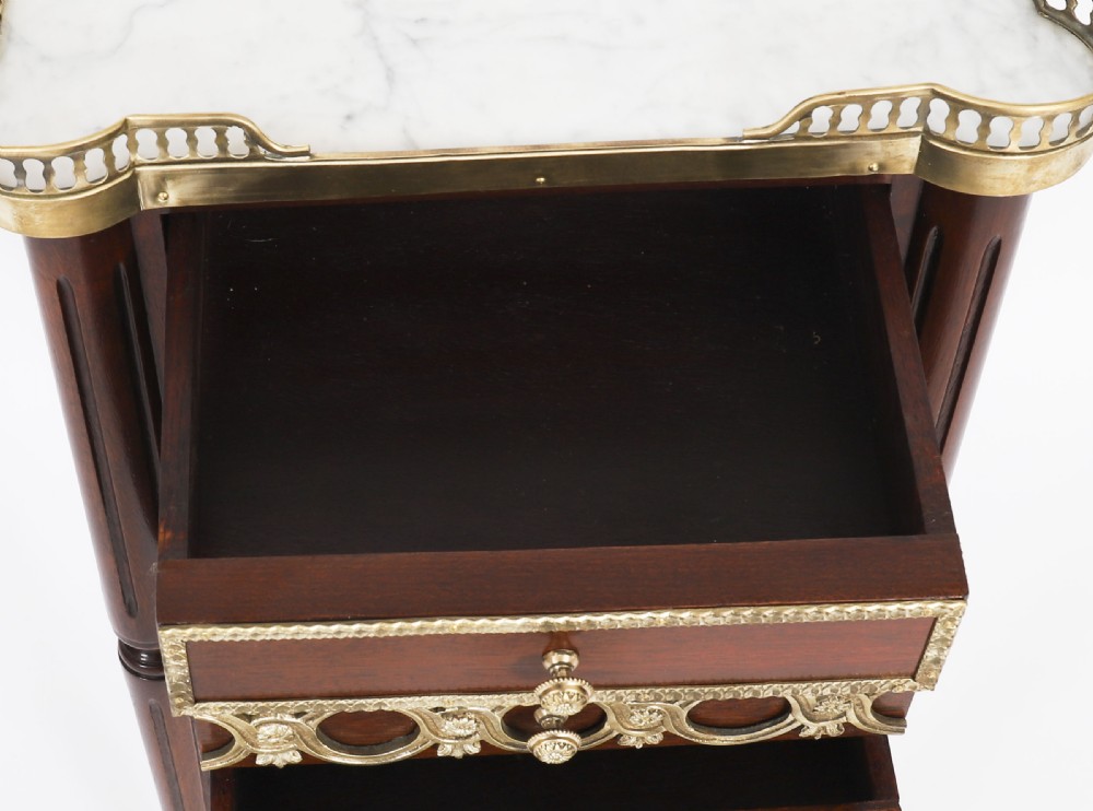 A pair of 19th-century mahogany French Empire bedside cabinets featuring white marble tops with pierced brass galleries, gilt bronze mounts, and slender fluted legs. View XVIII