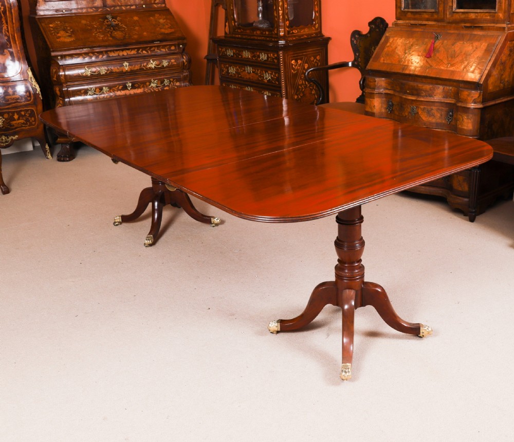 A George III Regency period mahogany twin pillar dining table featuring reeded edge detail and tripod pedestal legs with brass castors.