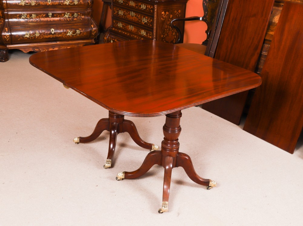 A George III Regency period mahogany twin pillar dining table featuring reeded edge detail and tripod pedestal legs with brass castors. View X