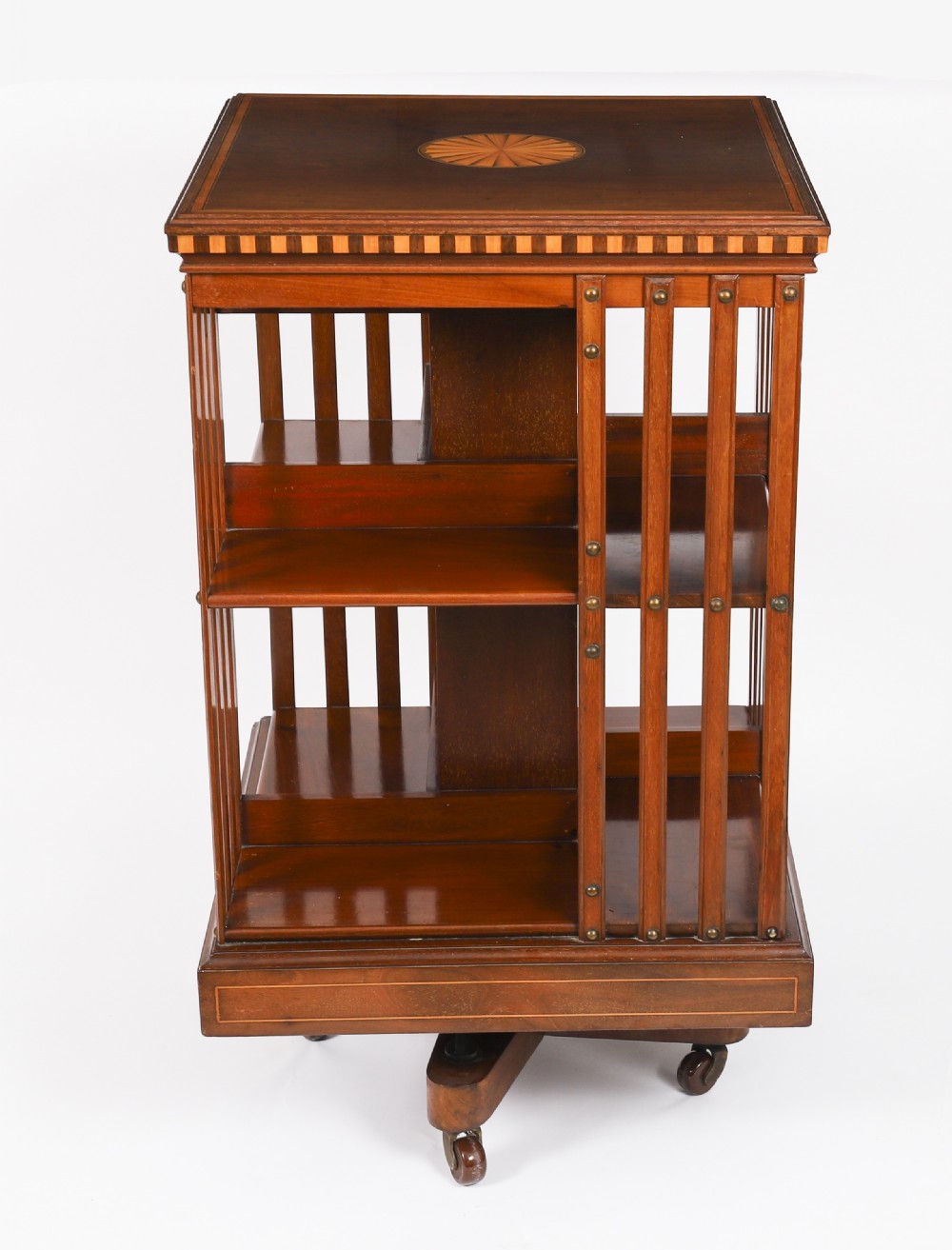 An Edwardian flame mahogany revolving bookcase featuring two tiers, vertical slatted sides with brass studs, satinwood inlay, and castors. View II