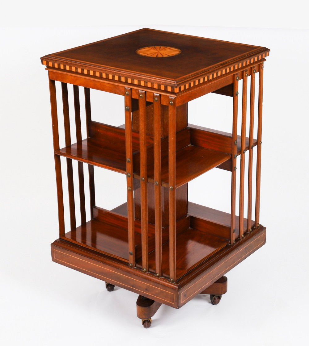 An Edwardian flame mahogany revolving bookcase featuring two tiers, vertical slatted sides with brass studs, satinwood inlay, and castors. View III