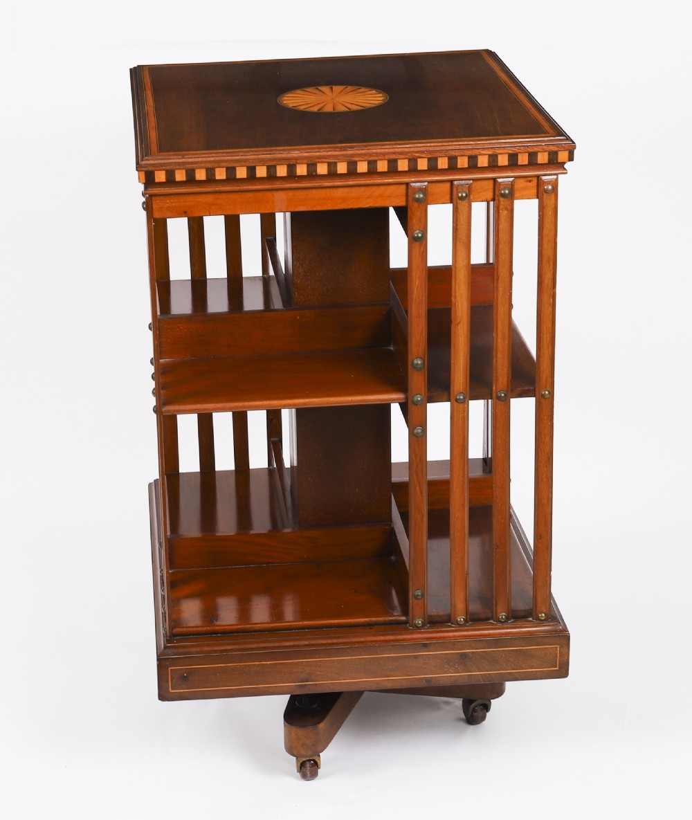An Edwardian flame mahogany revolving bookcase featuring two tiers, vertical slatted sides with brass studs, satinwood inlay, and castors. View V