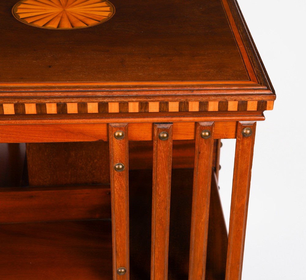 An Edwardian flame mahogany revolving bookcase featuring two tiers, vertical slatted sides with brass studs, satinwood inlay, and castors. View IX