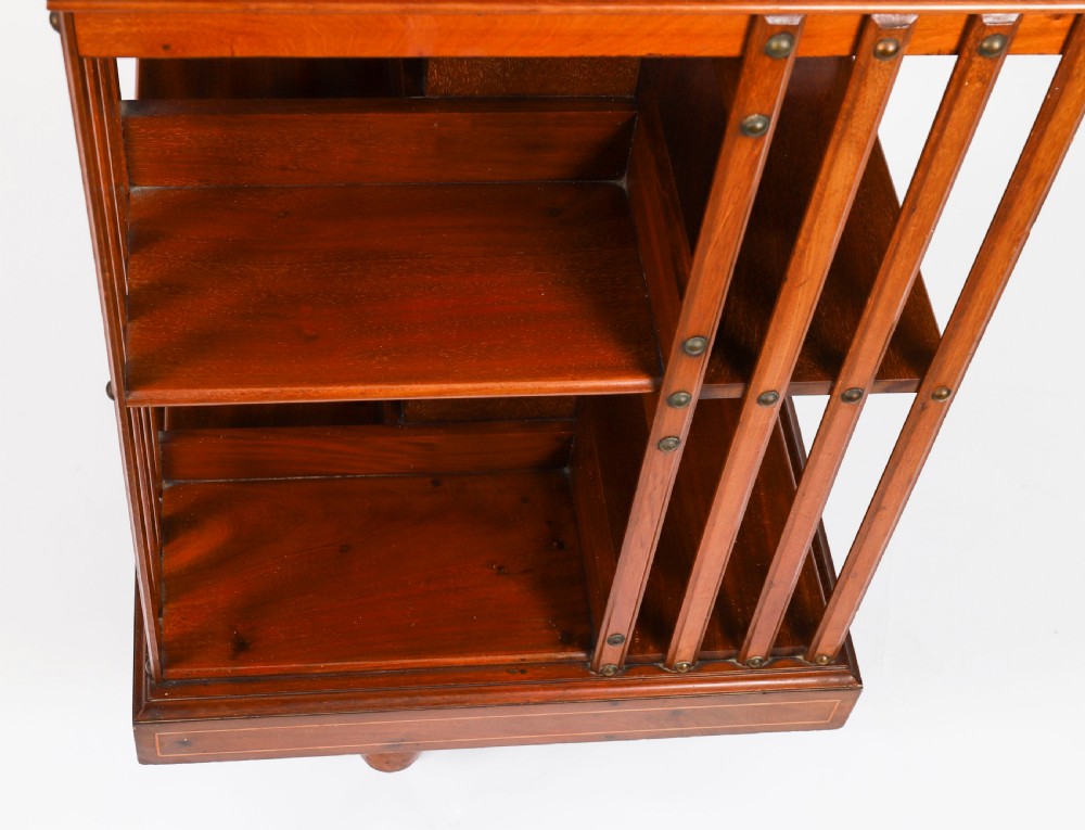 An Edwardian flame mahogany revolving bookcase featuring two tiers, vertical slatted sides with brass studs, satinwood inlay, and castors. View XI