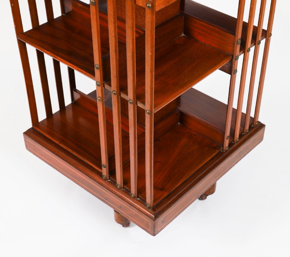 An Edwardian flame mahogany revolving bookcase featuring two tiers, vertical slatted sides with brass studs, satinwood inlay, and castors. View XII