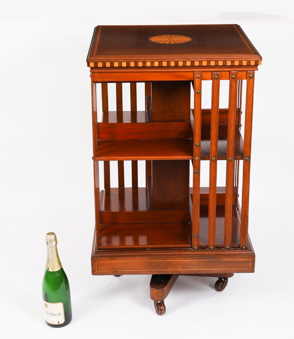 An Edwardian flame mahogany revolving bookcase featuring two tiers, vertical slatted sides with brass studs, satinwood inlay, and castors. View XIII