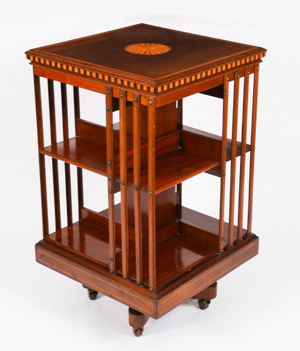 An Edwardian flame mahogany revolving bookcase featuring two tiers, vertical slatted sides with brass studs, satinwood inlay, and castors. View XIV