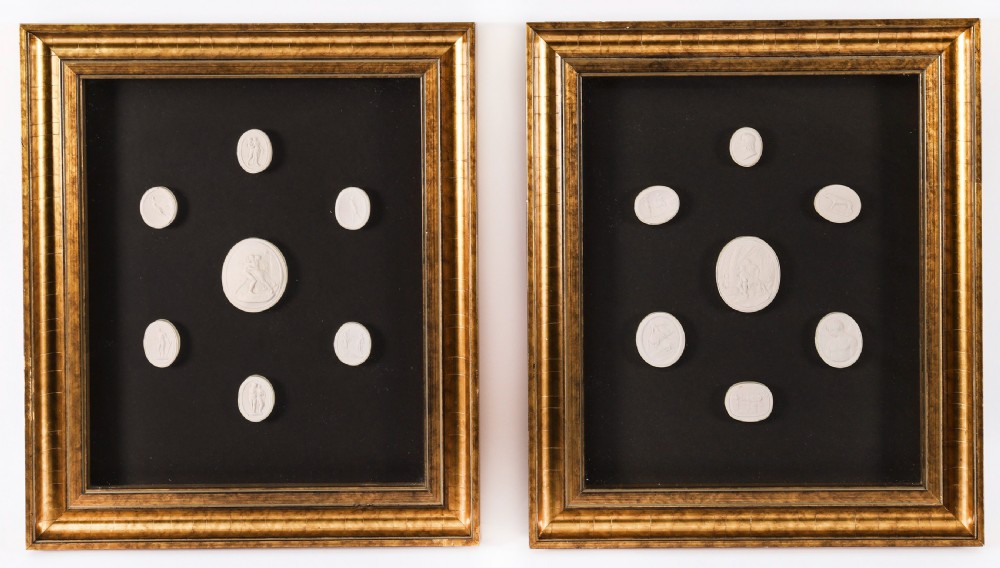 A pair of gold giltwood frames displaying classical white plaster intaglio casts arranged symmetrically against a dark background.