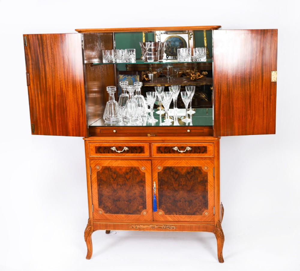 An Art Deco burr walnut cocktail cabinet featuring marquetry floral medallions, brass handles, two drawers, and cabriole legs against a white background. View III