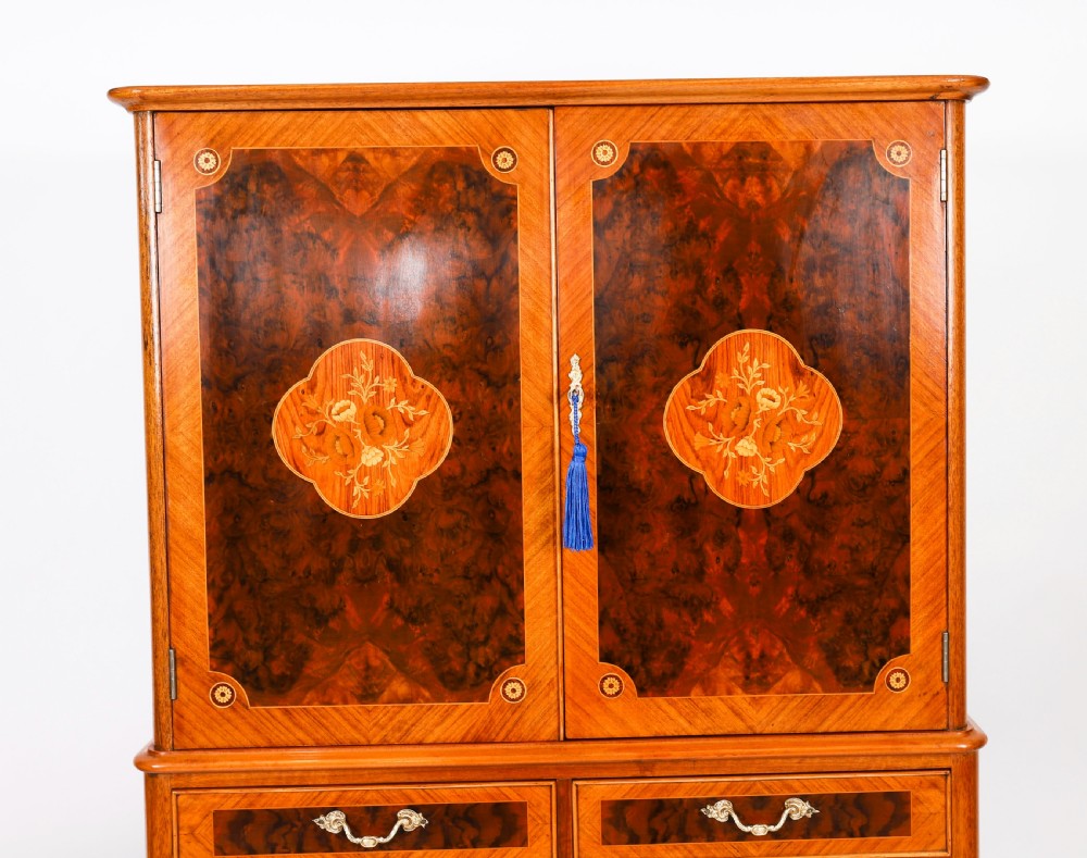 An Art Deco burr walnut cocktail cabinet featuring marquetry floral medallions, brass handles, two drawers, and cabriole legs against a white background. View V