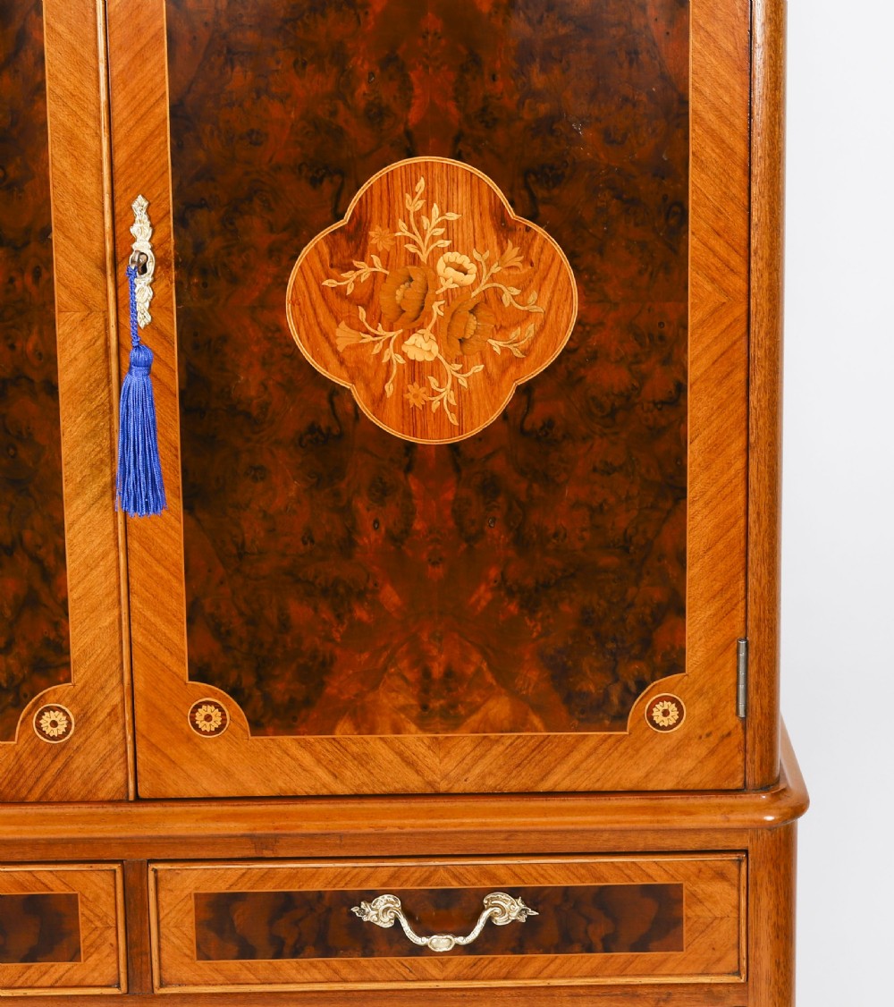 An Art Deco burr walnut cocktail cabinet featuring marquetry floral medallions, brass handles, two drawers, and cabriole legs against a white background. View VI
