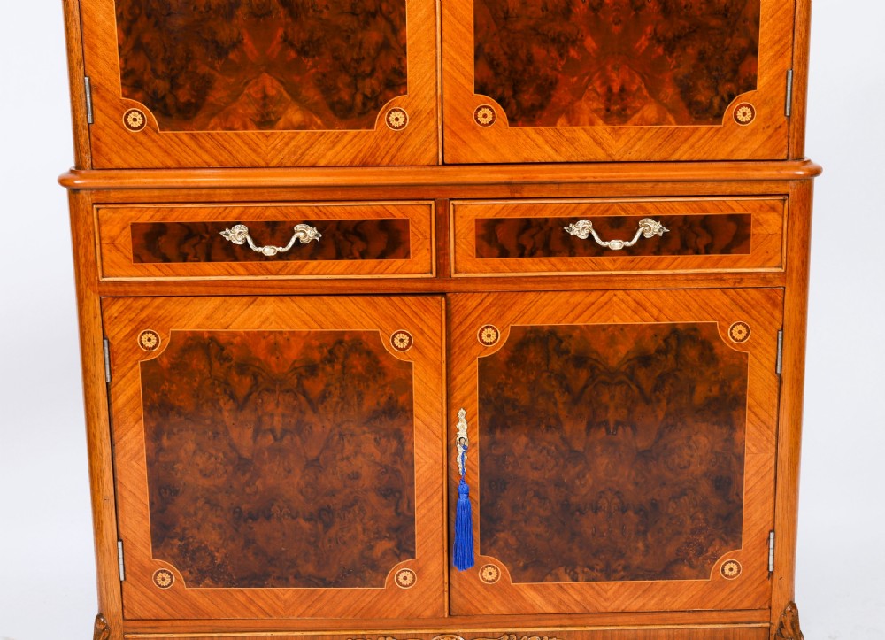 An Art Deco burr walnut cocktail cabinet featuring marquetry floral medallions, brass handles, two drawers, and cabriole legs against a white background. View IX