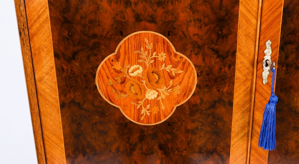 An Art Deco burr walnut cocktail cabinet featuring marquetry floral medallions, brass handles, two drawers, and cabriole legs against a white background. View X