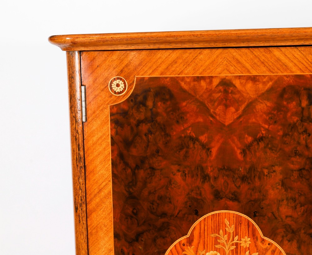 An Art Deco burr walnut cocktail cabinet featuring marquetry floral medallions, brass handles, two drawers, and cabriole legs against a white background. View XI