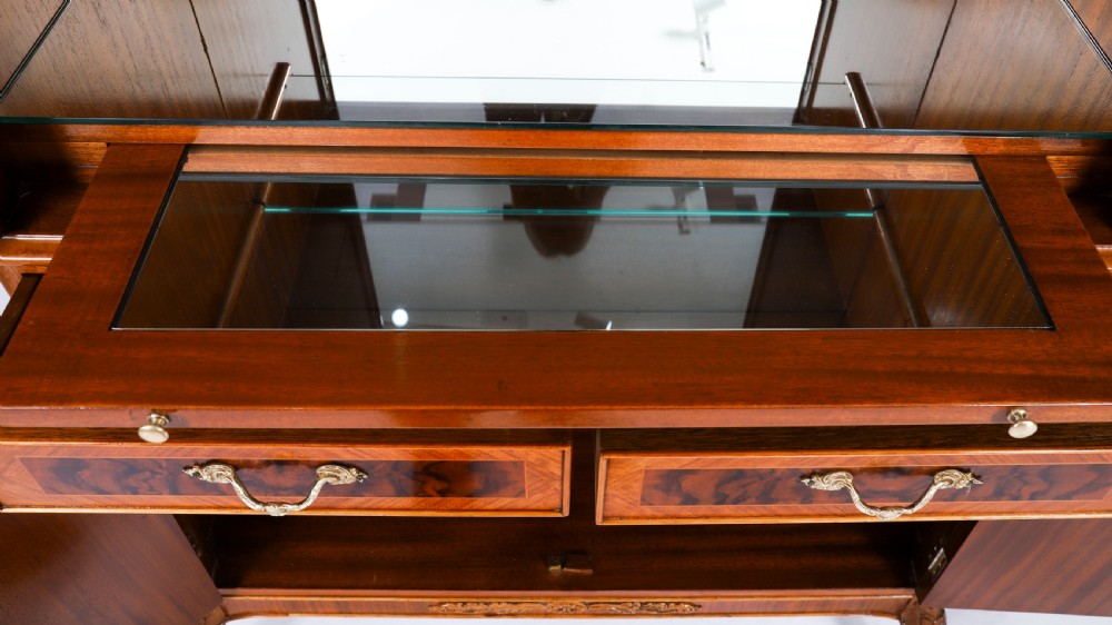 An Art Deco burr walnut cocktail cabinet featuring marquetry floral medallions, brass handles, two drawers, and cabriole legs against a white background. View XV