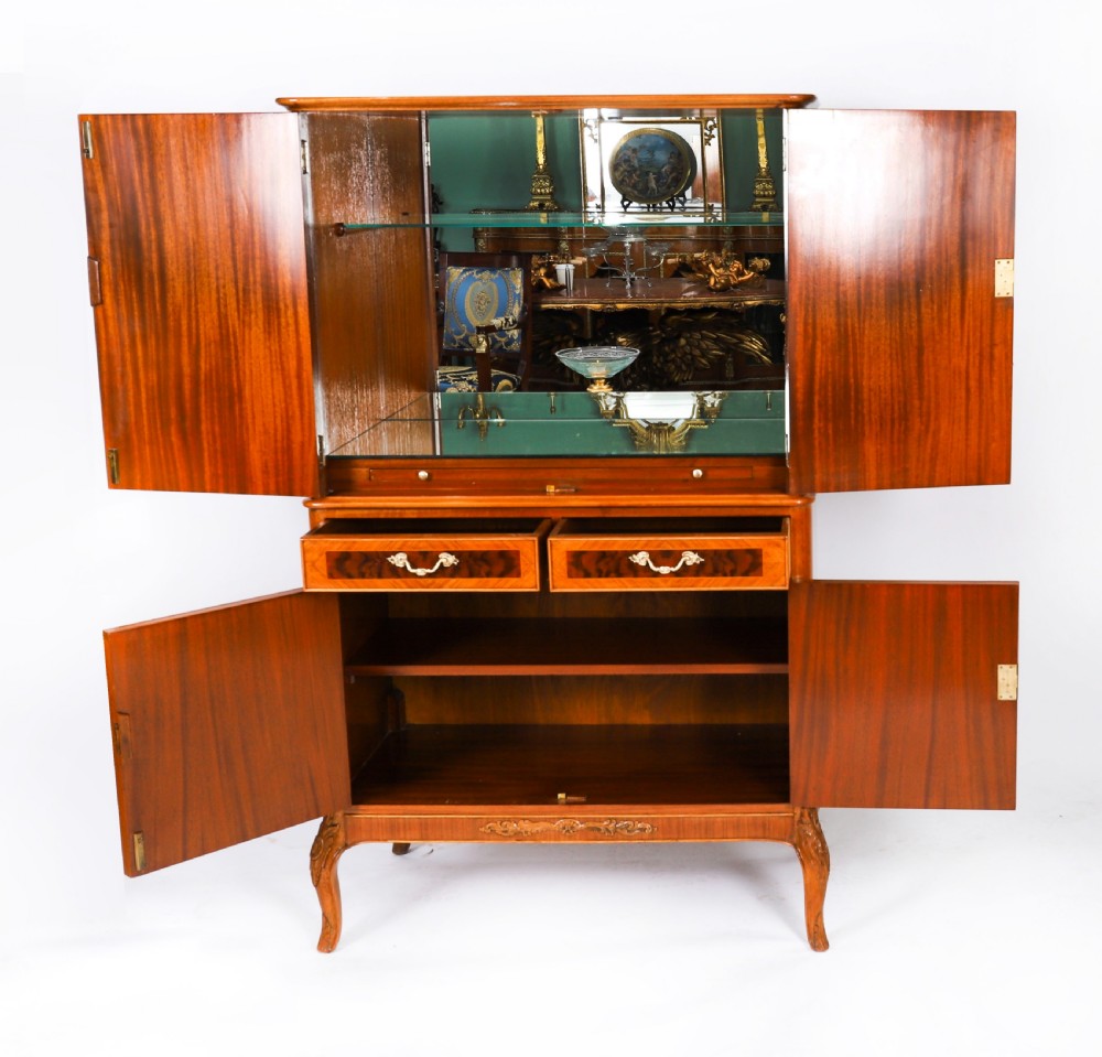 An Art Deco burr walnut cocktail cabinet featuring marquetry floral medallions, brass handles, two drawers, and cabriole legs against a white background. View XVI