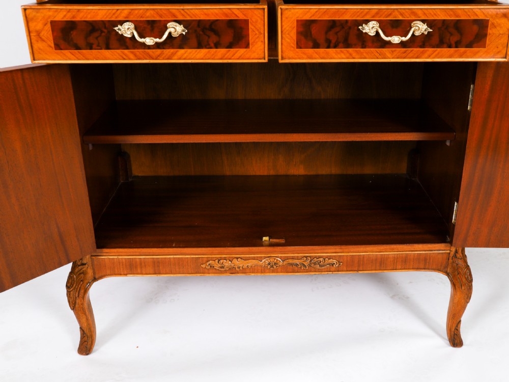 An Art Deco burr walnut cocktail cabinet featuring marquetry floral medallions, brass handles, two drawers, and cabriole legs against a white background. View XVII