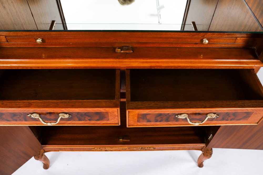 An Art Deco burr walnut cocktail cabinet featuring marquetry floral medallions, brass handles, two drawers, and cabriole legs against a white background. View XVIII