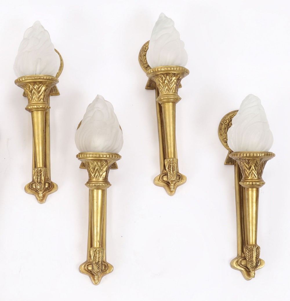 Set of four Neo-Classical style wall lights crafted in gilt metal with flaming torch backplates and frosted glass flame-shaped shades.