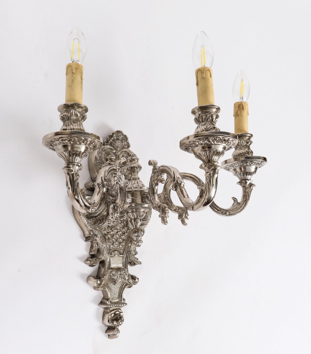 A matching set of four silver-plated three-arm French Rococo style wall appliques featuring ornate foliage scrollwork and candle-shaped bulb holders. View V