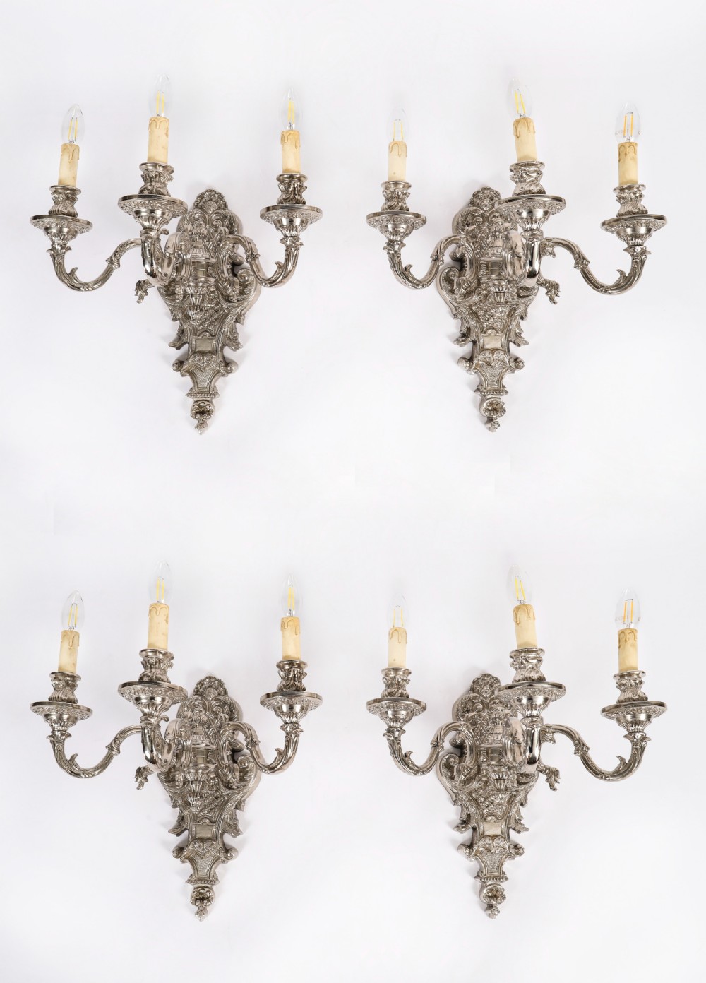 A matching set of four silver-plated three-arm French Rococo style wall appliques featuring ornate foliage scrollwork and candle-shaped bulb holders. View X