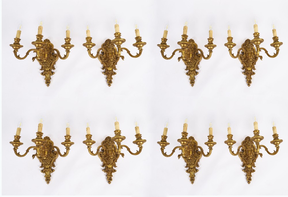 A set of eight French gilt bronze three-arm wall appliques featuring ornate foliate castings and candle-style fittings.
