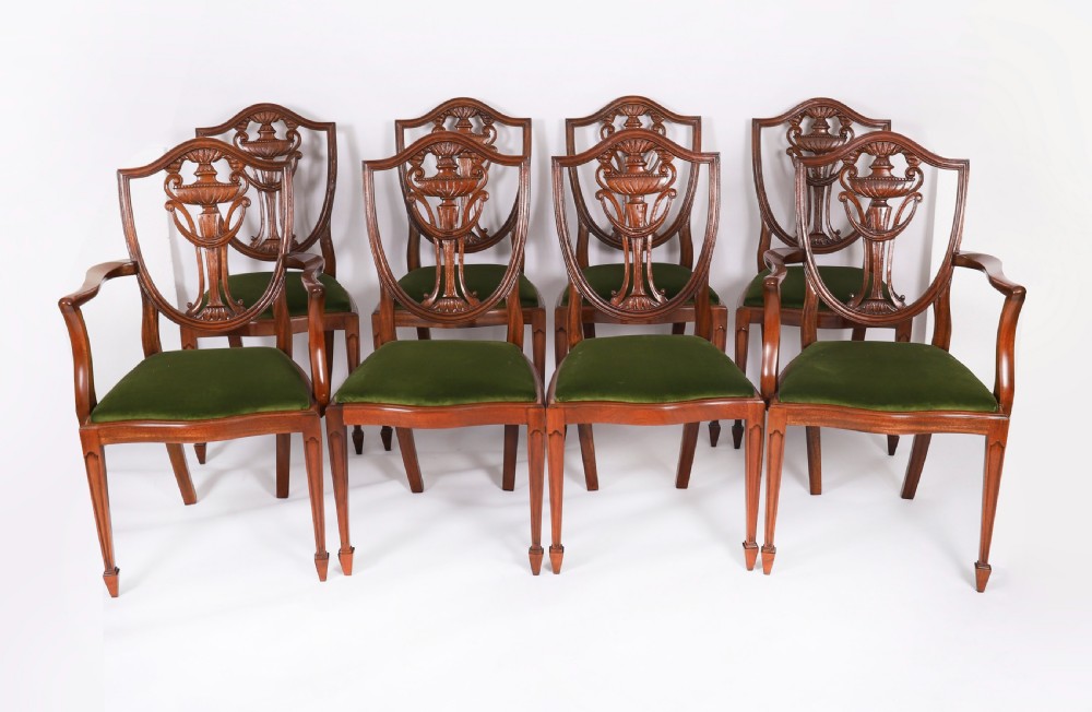 A set of eight Edwardian mahogany dining chairs featuring carved shield backs with urn splats and green velvet upholstered seats.
