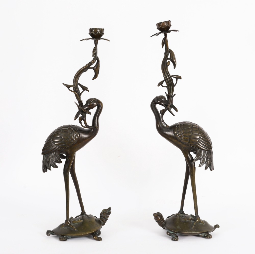 A pair of 19th-century Japanese dark bronze pricket candlesticks formed as cranes standing on tortoises holding lotus stems in their beaks.